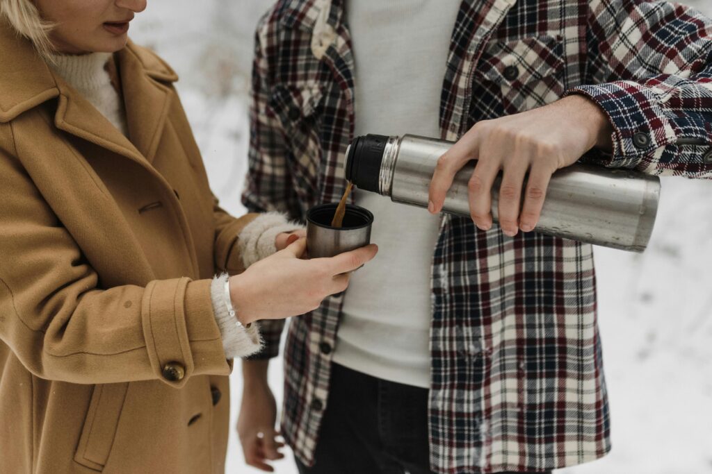 A couple pours hot coffee from a thermos during a cozy winter outing in the snow.